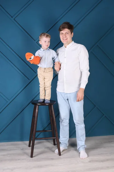 Jonge knappe vader en zoontje op kruk pose in blauwe studi — Stockfoto