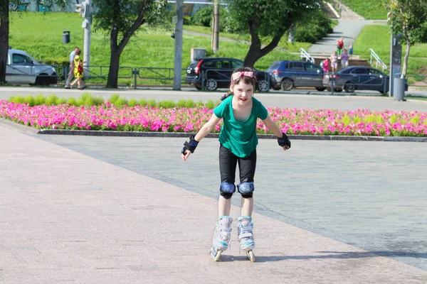 Glückliches Mädchen auf Rollschuhen auf sonnigem Stadtplatz mit Blumenbeet — Stockfoto