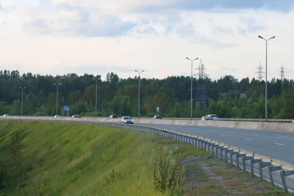 Багато сучасних автомобілів рухаються по сучасному шосе з ліхтарями влітку — стокове фото