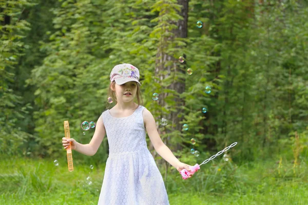 Šťastná dívka v čepici si hraje s mýdlovými bublinami v létě zelený park — Stock fotografie