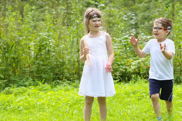Mooi meisje en jongen spelen met zeepbellen in zomer groen fores — Stockfoto
