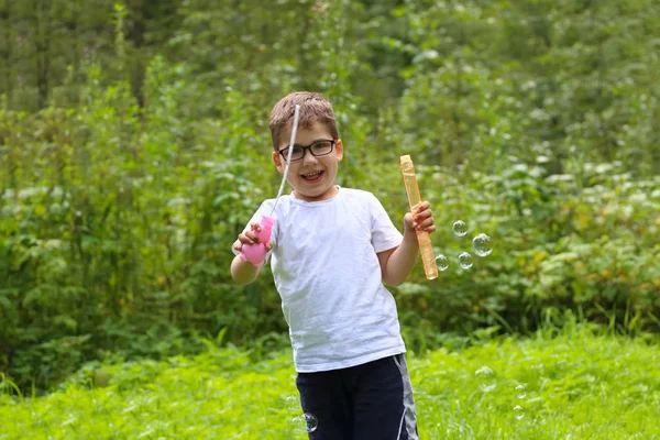 Szczęśliwy mały chłopiec w okularach odgrywa z baniek mydlanych w lecie fo — Zdjęcie stockowe