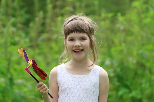 Niña en sonrisas blancas y sostiene molino de viento en verano verde f —  Fotos de Stock