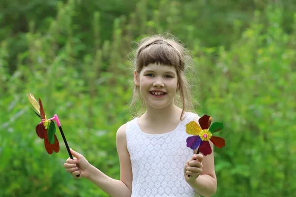 Маленькая красивая девочка с двумя ветряными мельницами игрушки летом зеленые форели — стоковое фото