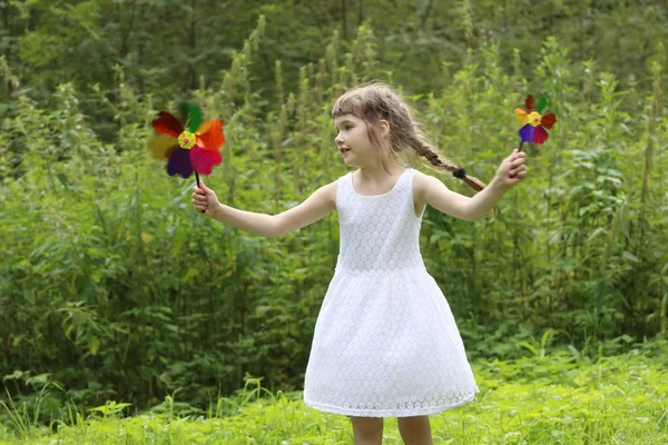 Pretty little girl with two windmills spins in summer green fore — Stock Photo, Image