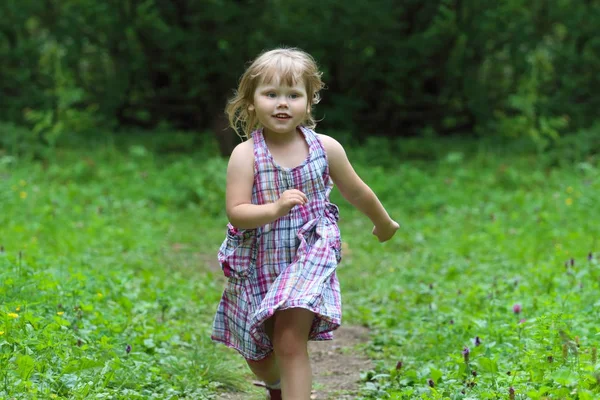 Sorridente bambina in abito corre al giorno d'estate nel parco verde — Foto Stock