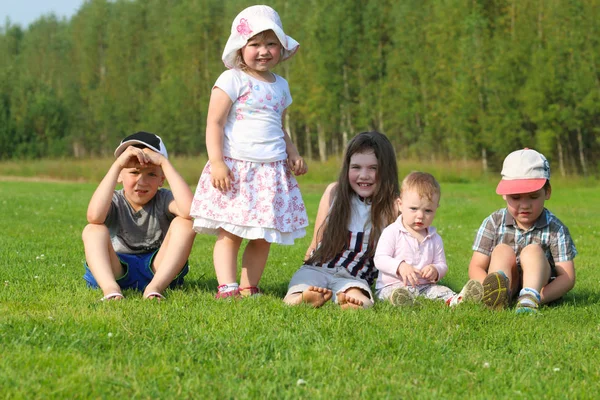 Five happy children sit and stand on green grass on summer field — Stock Photo, Image