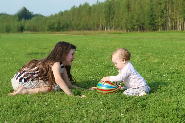 Girl plays with baby and ball on green field at summer evening — Stock Photo, Image