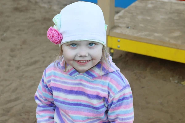 Piccola bella ragazza in cappello sorride sul parco giochi per bambini — Foto Stock
