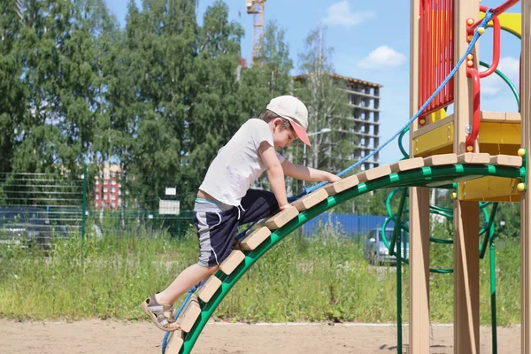Malý kluk v čepici šplhá na dětské hřiště na léto — Stock fotografie