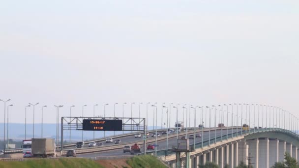 Carros, ônibus e caminhões se movem na ponte com a placa do tempo, tradução de texto - Rio Kama — Vídeo de Stock