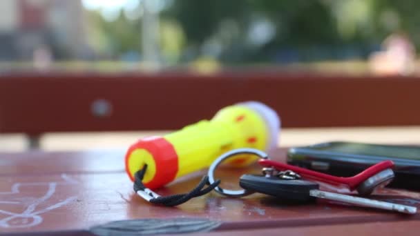Sleutel, smartphone en Zaklamp sleutelhanger op tafel liggen buiten op een zomerdag — Stockvideo