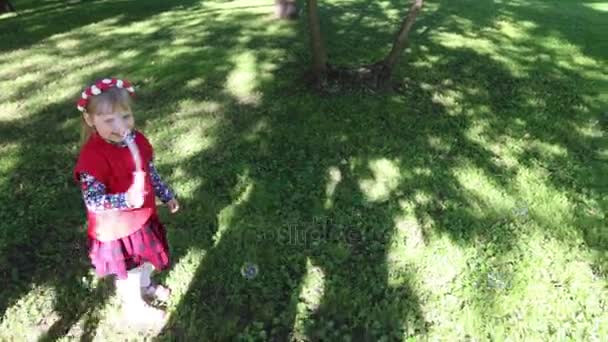 Счастливая маленькая девочка делает мыльные пузыри в зеленом летнем парке — стоковое видео