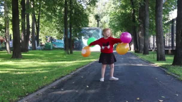 Bonne petite fille en jupe tourne avec des ballons lumineux dans le parc d'été vert — Video