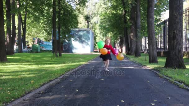 Glückliches kleines Mädchen im Rock rennt und springt mit Luftballons im grünen Sommerpark — Stockvideo