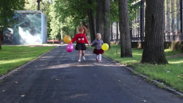 Twee gelukkige kleine meisjes lopen met ballonnen in groene zomer park — Stockvideo