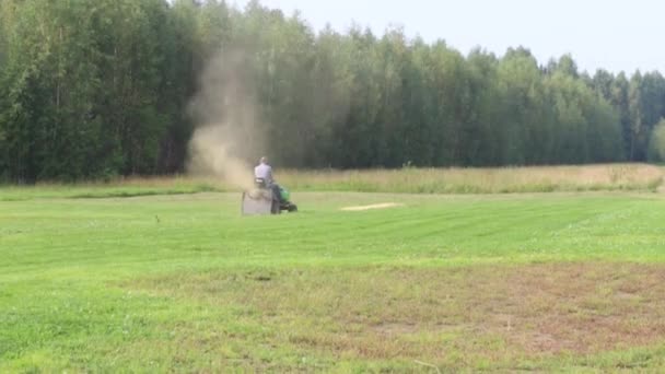 Traktorek kosiarka pracuje na duży zielony pole w pobliżu lasu w lato — Wideo stockowe