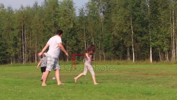 Père, fils et fille jouent avec le ballon sur le terrain vert avec la porte de football à l'été — Video