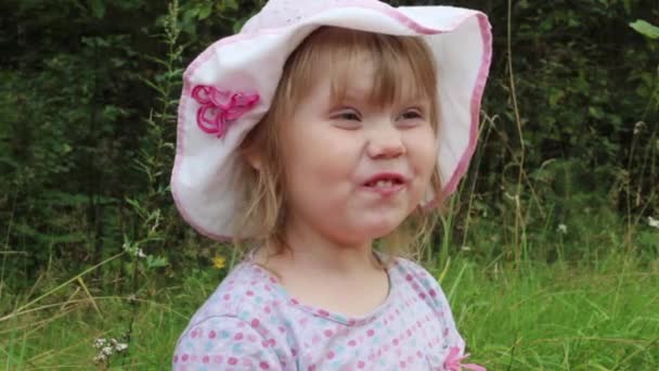 Funny little girl in hat grimaces among grass in summer park — Stock Video