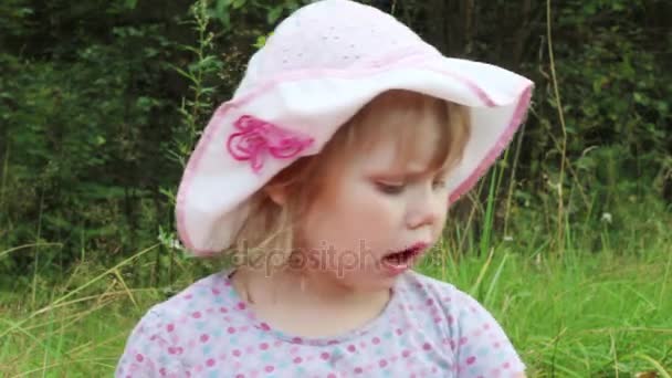 Little girl in hat eats among grass in summer park — Stock Video