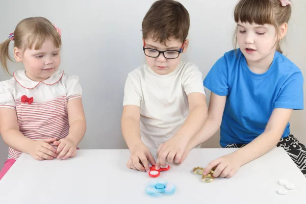 Two happy girls and boy play with spinners on table in white stu — Stock Photo, Image