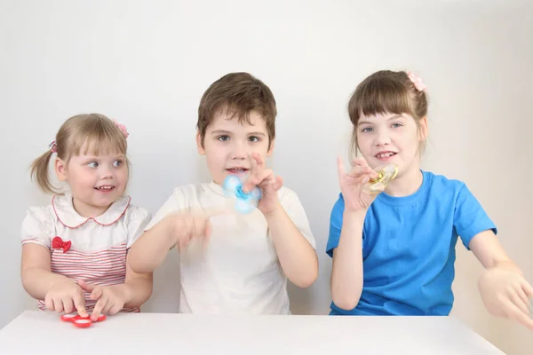 Tres niños felices juegan con hilanderos en la mesa en un estudio blanco — Foto de Stock