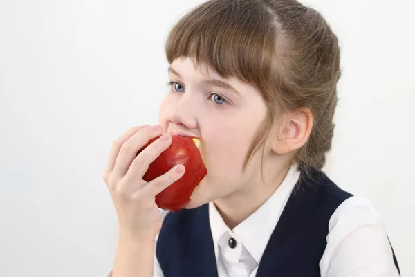 Portrait of pretty schoolgirl in uniform eating red apple — Stock Photo, Image