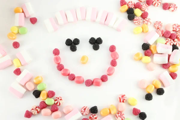 Many sweet candies and marshmallows in face shape on white surfa — Stock Photo, Image