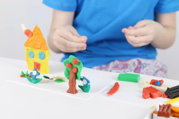 Manos de niño moldeando casa brillante, árbol, flores de plastilina — Foto de Stock