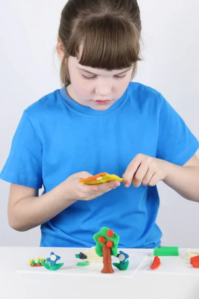 Mooi meisje mallen speelgoed uit de plasticine op witte tafel in whit — Stockfoto