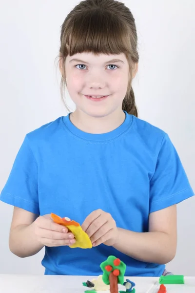 Hermosa chica feliz moldes juguetes de plastilina en la mesa blanca i — Foto de Stock