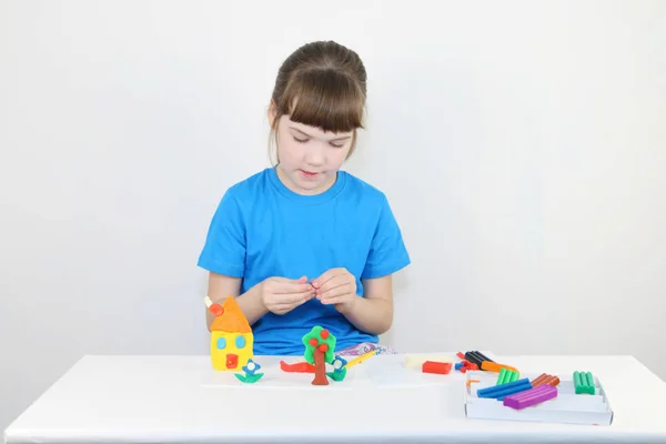 Pretty girl in blue molds house from plasticine on white table i