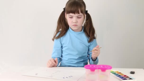 Улыбающаяся девушка в синей акварели рисует бабочку на столе в белой комнате — стоковое видео