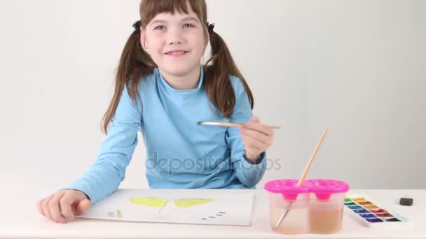 Usmívající se dívka akvarel maluje motýl na stole v bílé místnosti