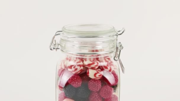 Vaso di vetro con molte caramelle dolci luminose su sfondo bianco — Video Stock