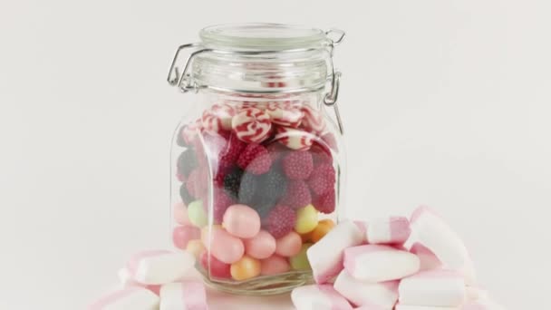 Glass jar with many bright sweet candies and marshmallows on white background — Stock Video