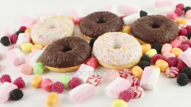 Donuts e doces brilhantes e marshmallows na mesa branca — Vídeo de Stock