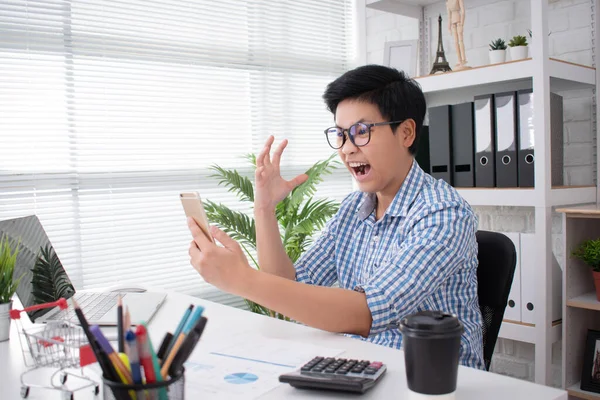 Um jovem empresário asiático mostra um rosto chocante de um smartphon — Fotografia de Stock