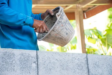 İnşaat işçileri gri tuğlalardan ve çimentodan yapılmış evler inşa ediyorlar. Çimento kovası ve ekipman taşımaya hazır.