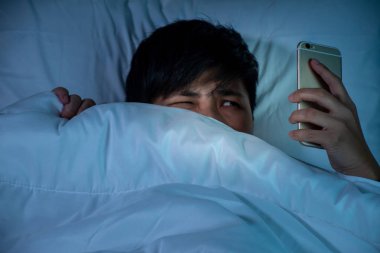Asyalı gençler gece yatağında akıllı telefon kullanıyor..