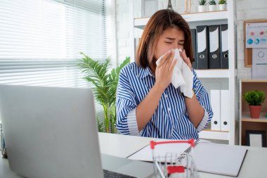 Asyalı bir işadamı ofisteki masasında hapşırıyor ve öksürüyor..