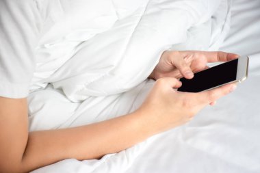 Odadaki yatakta akıllı telefon kullanarak Asyalı bir elin fotoğrafını çek..