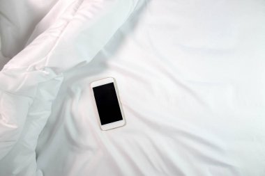 Kopya alanı olan beyaz bir yataktaki akıllı telefonun üst görüntüsü.