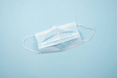 Virüsün yayılmasını engellemek için tıbbi bir maskenin üst görüntüsü. Mavi bir arkaplanda
