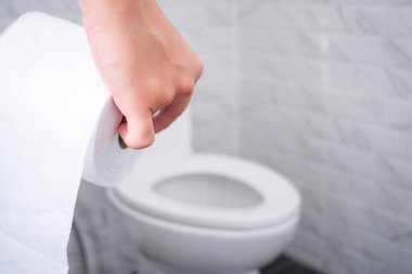 Asyalı eller tuvalet kağıdı rulolarını tutarak tuvalete gidiyor. Arka plan banyo..