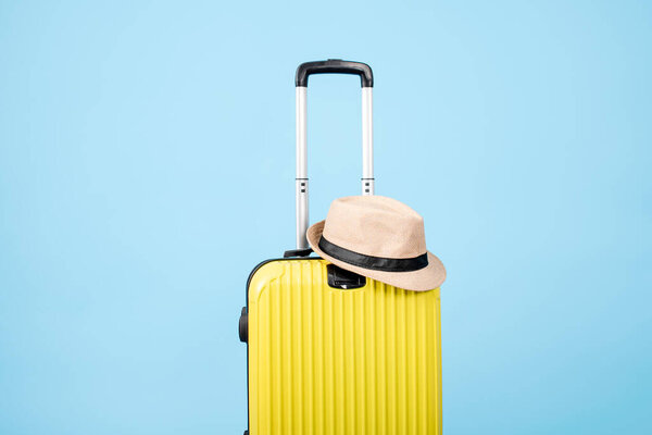A yellow suitcase with a hat on a blue background.