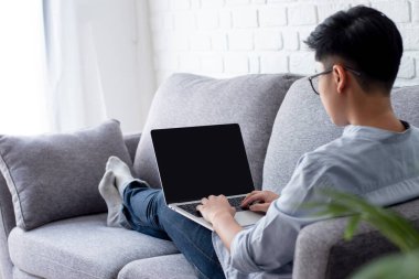 Gözlüklü yakışıklı evde kanepede yatarken dizüstü bilgisayar kullanıyor..