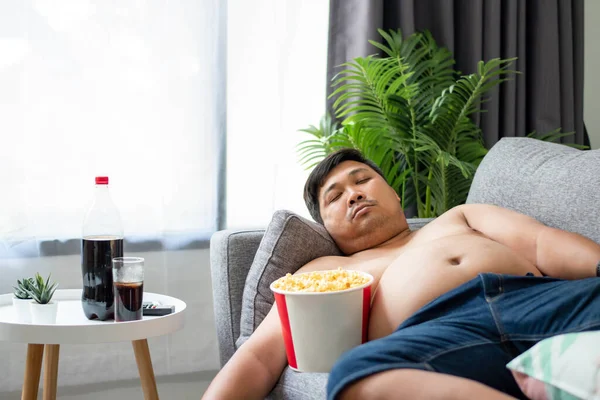 Fat man sleeps with popcorn on the sofa at home.