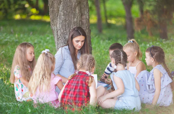 children hold a lesson with the teacher in the park on a green l