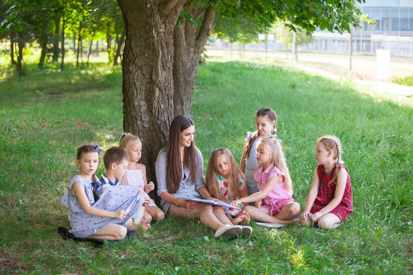 children hold a lesson with the teacher in the park on a green l